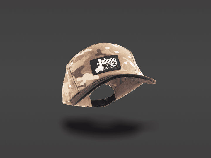 A desert camouflage 5-panel cap with a black patch on the front that reads &